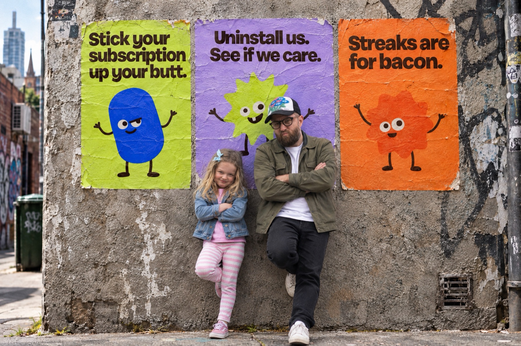John and Arlo leaning on a laneway wall under three Dash Dash Dash posters, both with their arms crossed, looking very cool